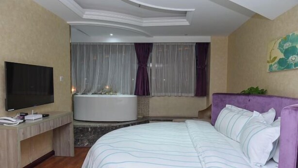 A hotel room with a bed, a TV, a desk, and a bathtub.