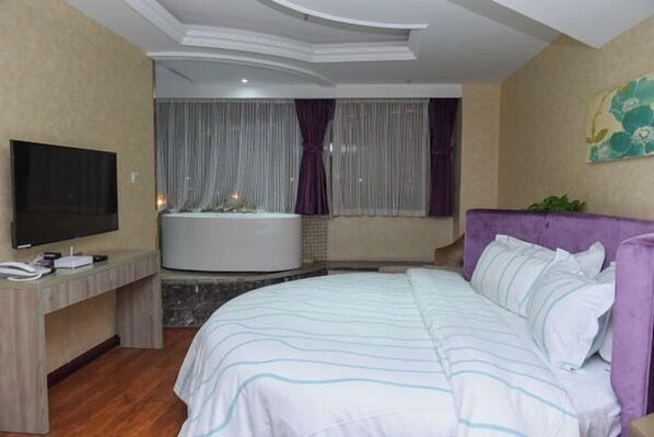 Quarto de hotel com cama, televisão, escrivaninha e banheira.
