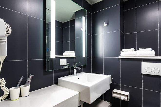 Ein modernes Badezimmer mit einem großen Spiegel, zwei Waschbecken, einem Föhn und einem Handtuchhalter.