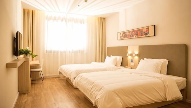 Habitación de hotel con dos camas, un escritorio, una silla, un televisor y una ventana con cortinas.
