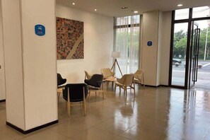 Un espace d’accueil avec des sièges, une œuvre d’art accrochée au mur et une porte vitrée donnant sur l’extérieur.