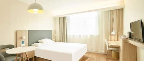 A hotel room with a bed, a desk with a chair, a television, and a window with curtains.
