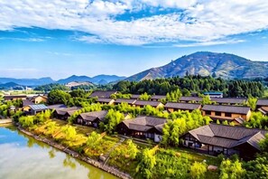 A row of traditional-style buildings with a river in the foreground and mountains in the background. - Sante Langkou Club (Chongyang)