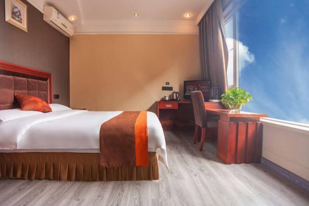 A hotel room with a bed, desk, chair, and a large window.