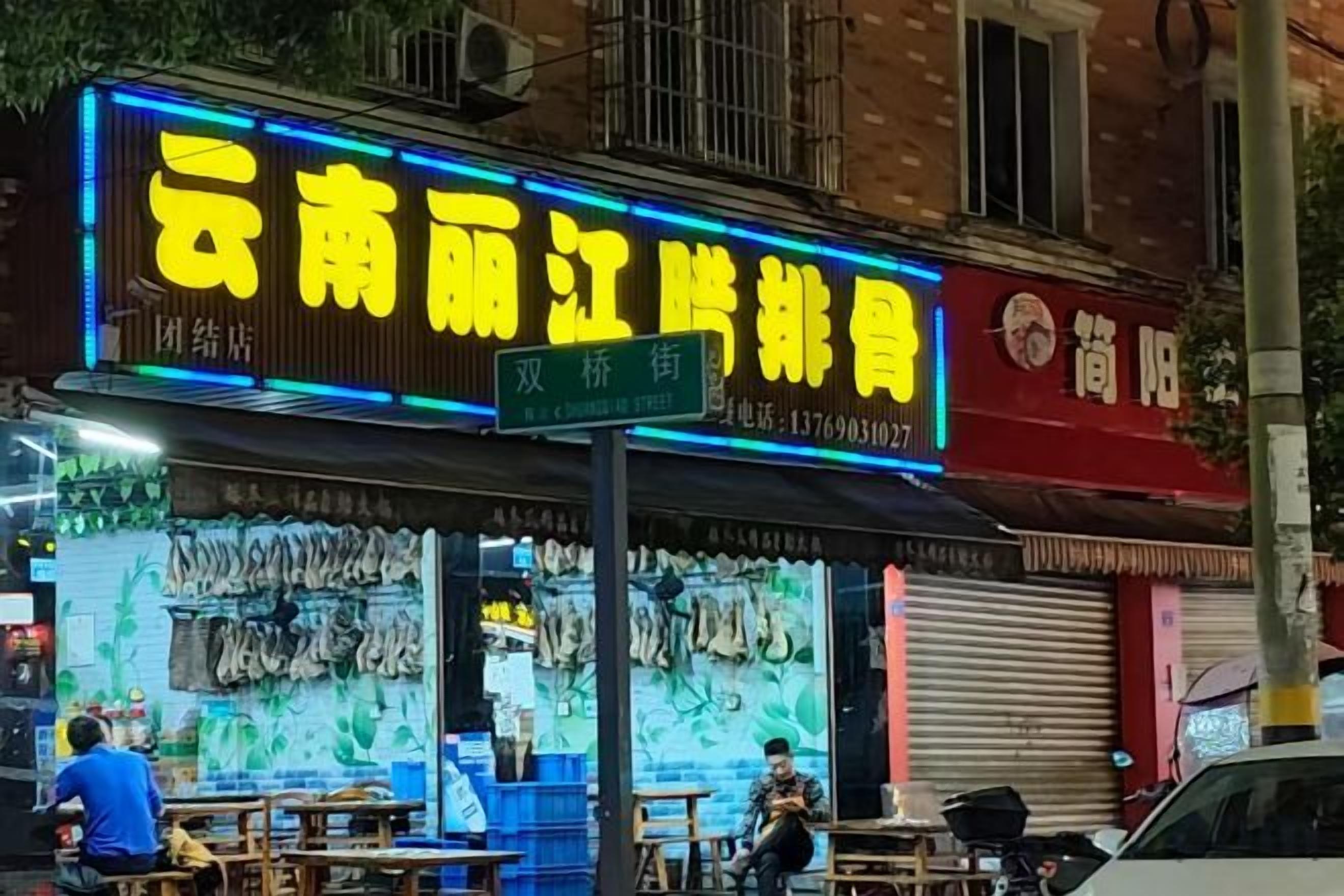 Un restaurant situé au bord de la rue, avec une terrasse et une enseigne au néon.