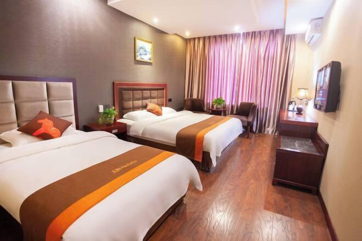 A hotel room with two beds, a wooden floor, a TV, and a window with curtains.