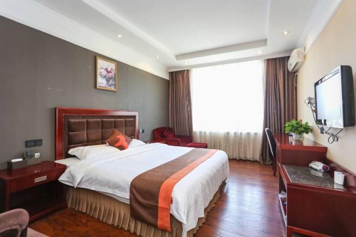 A hotel room with a large bed, a desk, a chair, a TV, and a window with curtains.