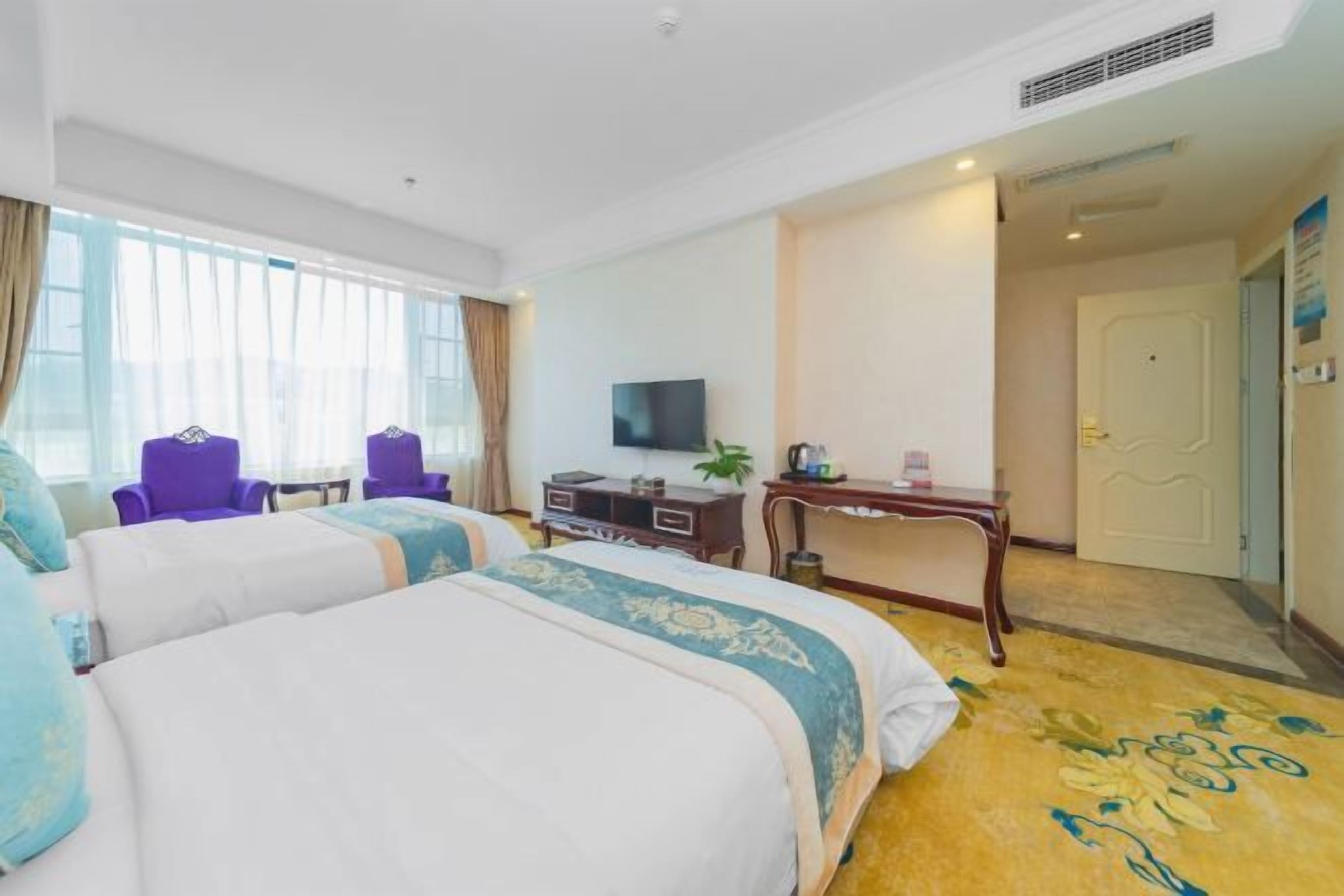 A hotel room with two beds, a TV, a desk, and a door.