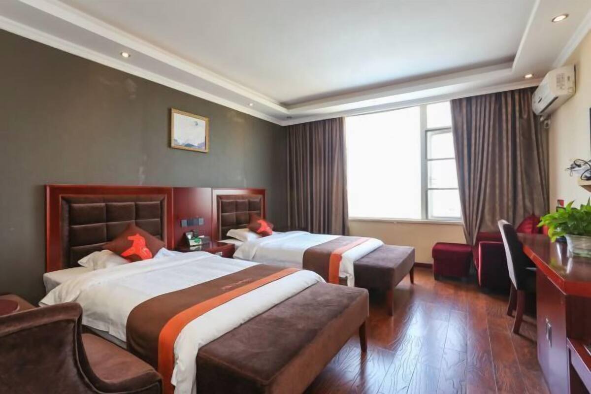 A hotel room with two beds, a desk, and a window.