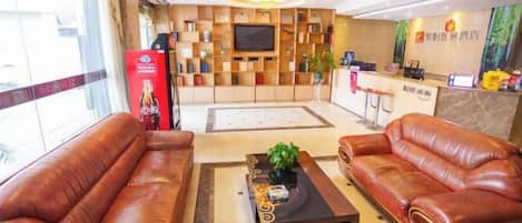 A hotel lobby with leather sofas, a coffee table, a reception desk, and a TV screen.