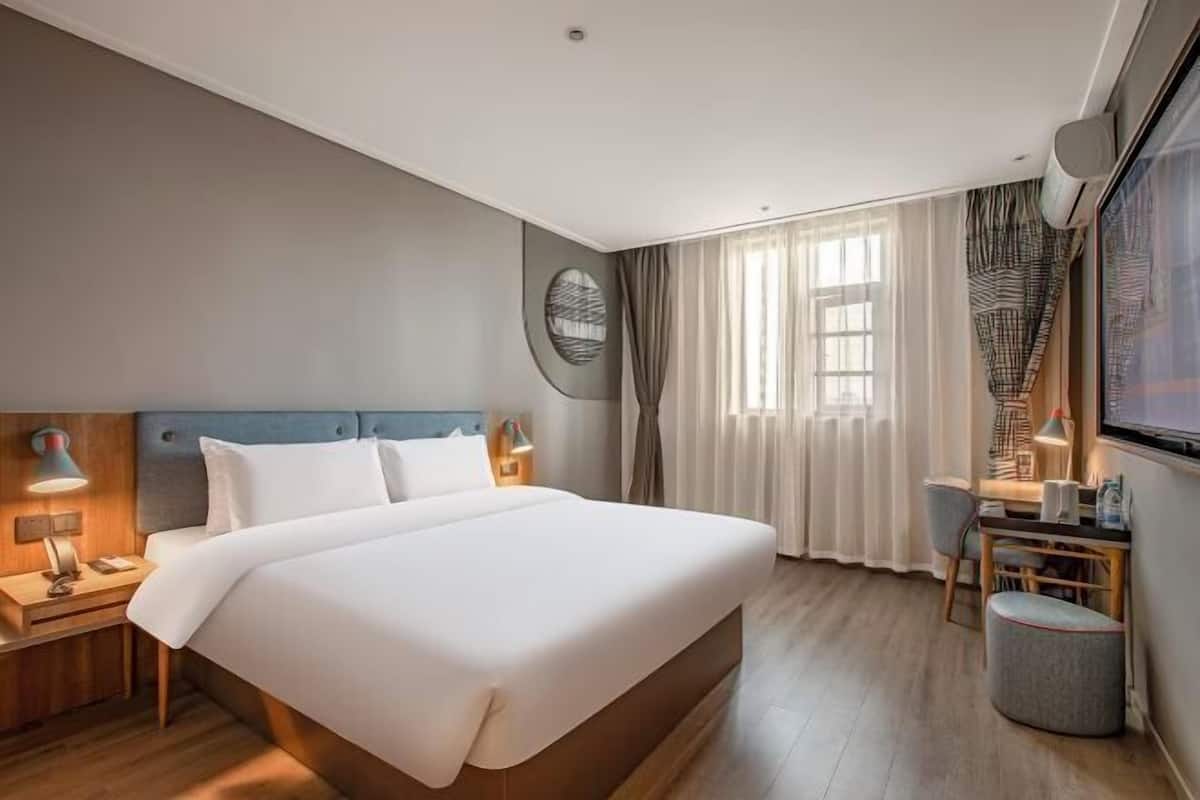 A hotel room with a large bed, a desk with a chair, a small table, and a TV.