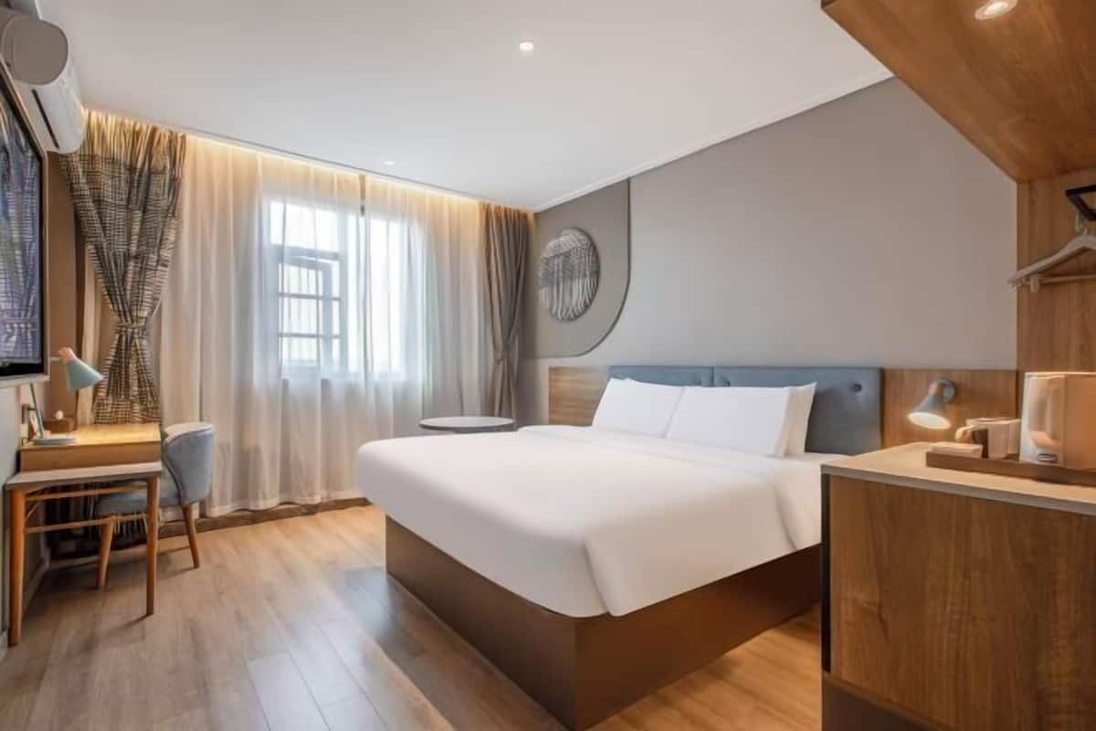 A modern hotel room with a large bed, a desk, and a small round table.