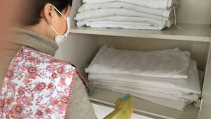 A person wearing a floral vest and gloves, organizing folded white towels on a shelf. - Jixi School Hotel (Jixi)