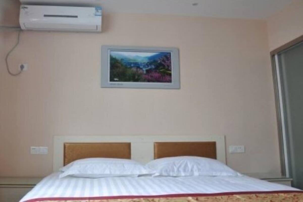 Een hotelkamer met een bed, een airconditioner, een lijst met een foto aan de muur en een raam.