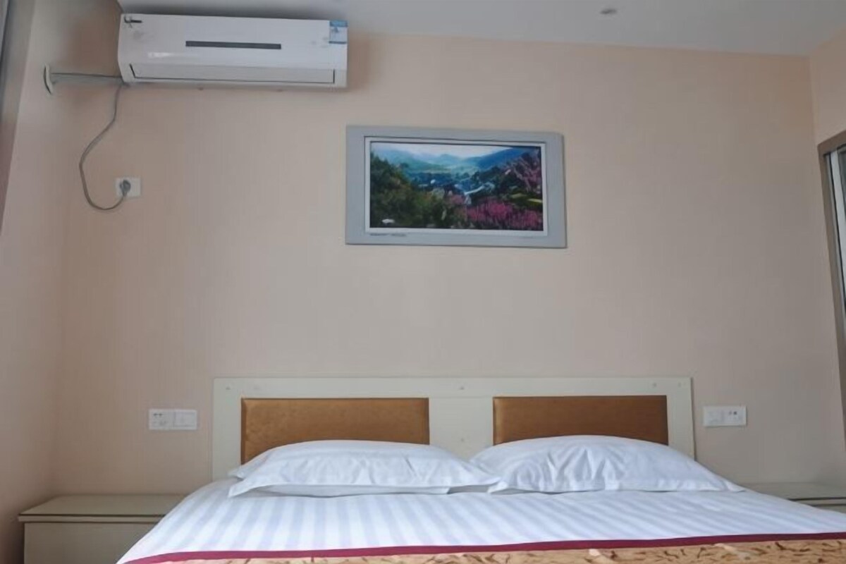 A hotel room with a bed, an air conditioning unit, a television mounted on the wall, and a window.