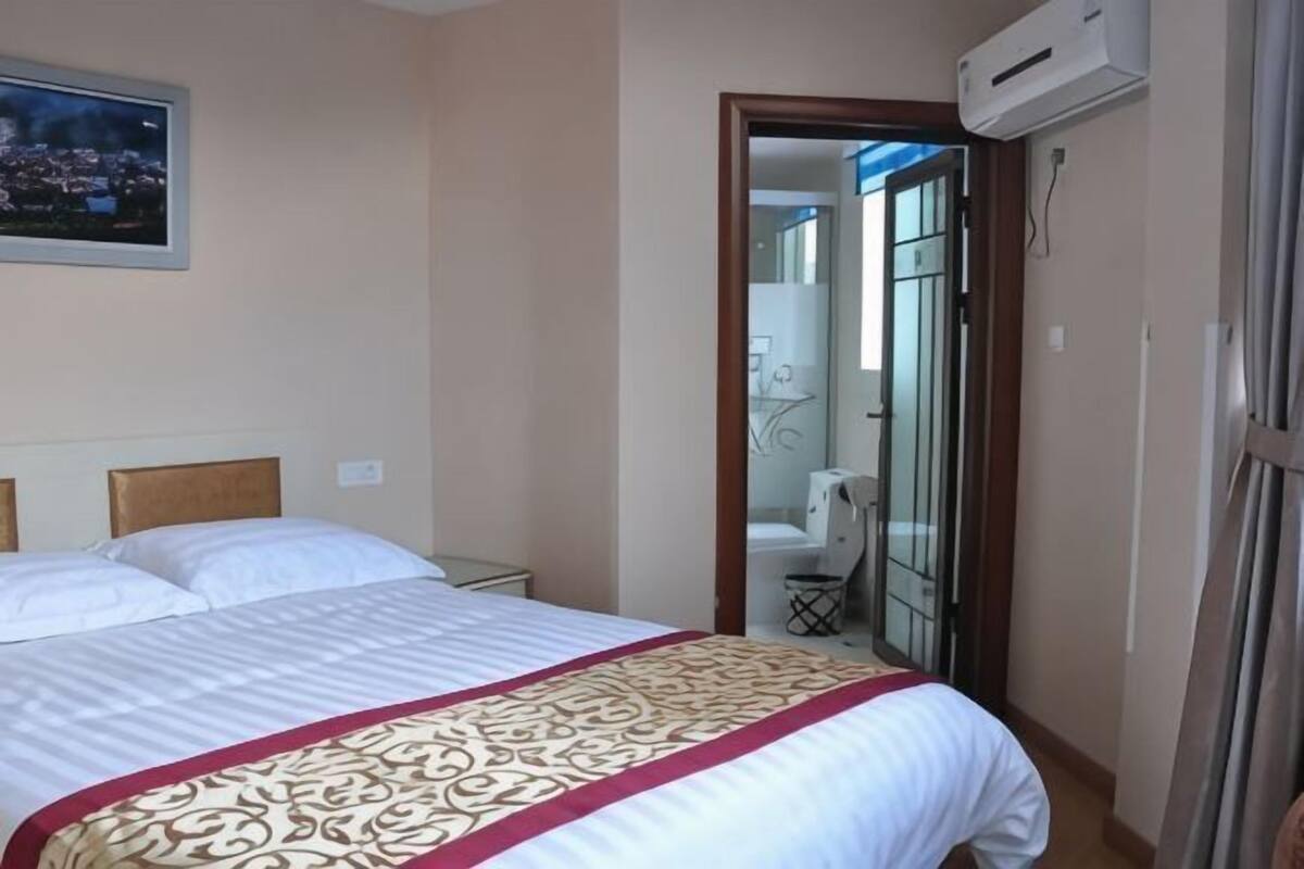 Een hotelkamer met een bed, een deur naar een badkamer en een airconditioner aan de muur.