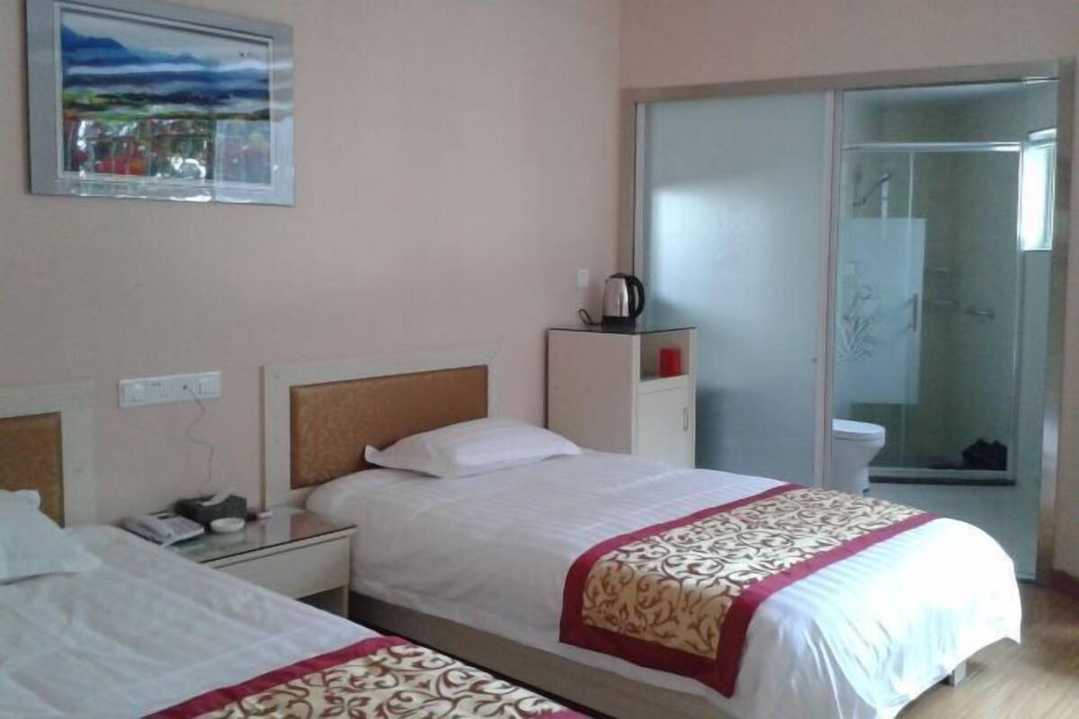 Hotelkamer met twee bedden, een glazen douchecabine, een schilderij aan de muur en een klein kastje met een waterkoker.