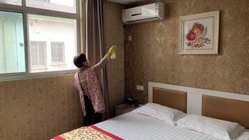 A hotel room with a bed, a window, an air conditioning unit, and a framed picture on the wall.