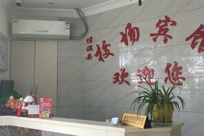 Una recepción con una planta en maceta, un cartel y texto rojo en la pared.