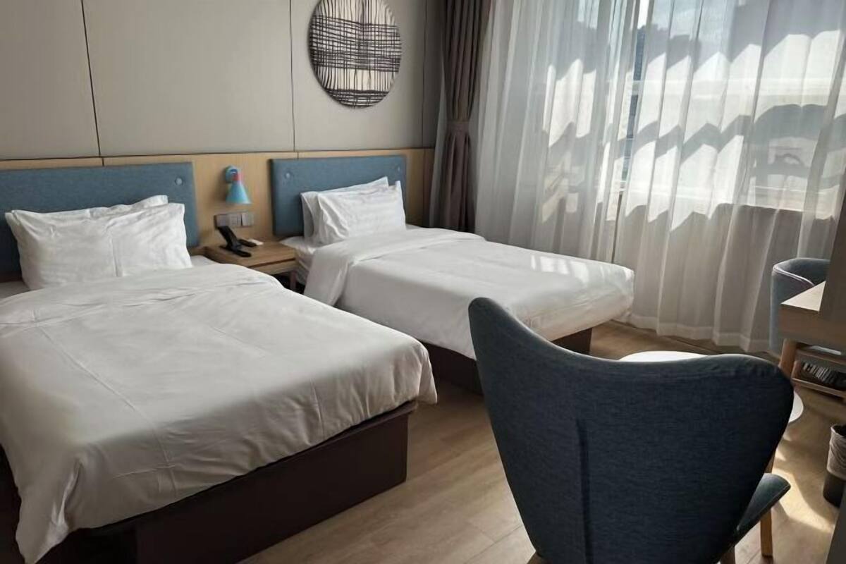 A hotel room with two beds, a desk, a chair, and a large window with curtains.