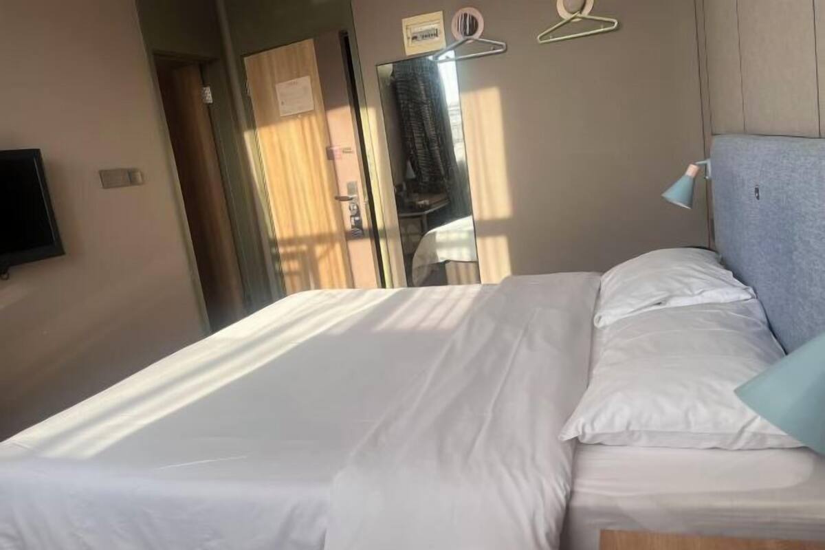 A hotel room with a bed, a mirror, a wall-mounted TV, and a window with curtains.