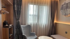 A modern room with a grey chair, a small round table, a bench, a window with sheer curtains, and a wall-mounted light fixture. - Homeinn · neo (Nanchang Xianghu Wetland Park Jiangling Subway Station) (Nanchang)