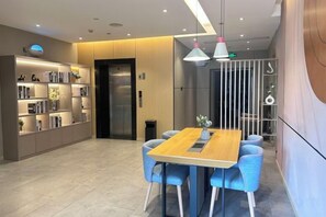 Een modern interieur met een eethoek, bestaande uit een houten tafel, blauwe stoelen, een boekenkast en een wandlamp.