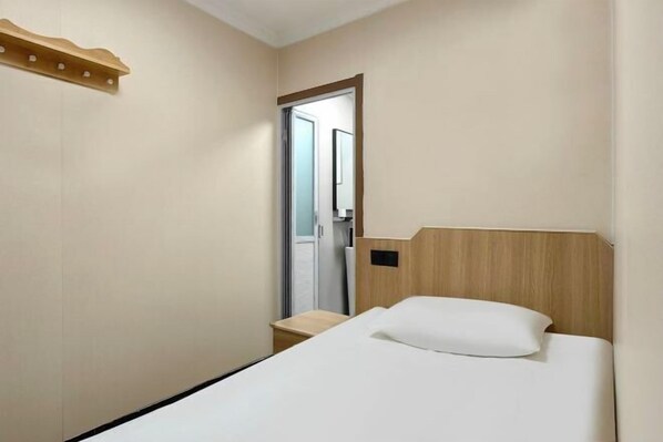 A hotel room with a single bed, a wooden headboard, a small bedside table, and a door leading to a bathroom. - Haoyun Hotel (Nanshida People's Hospital) (Nanjing)