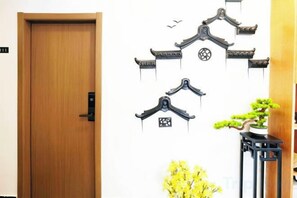 A wooden door, wall-mounted black traditional-style hooks, and a potted plant with yellow flowers. - Haoyun Hotel (Nanshida People's Hospital) (Nanjing)