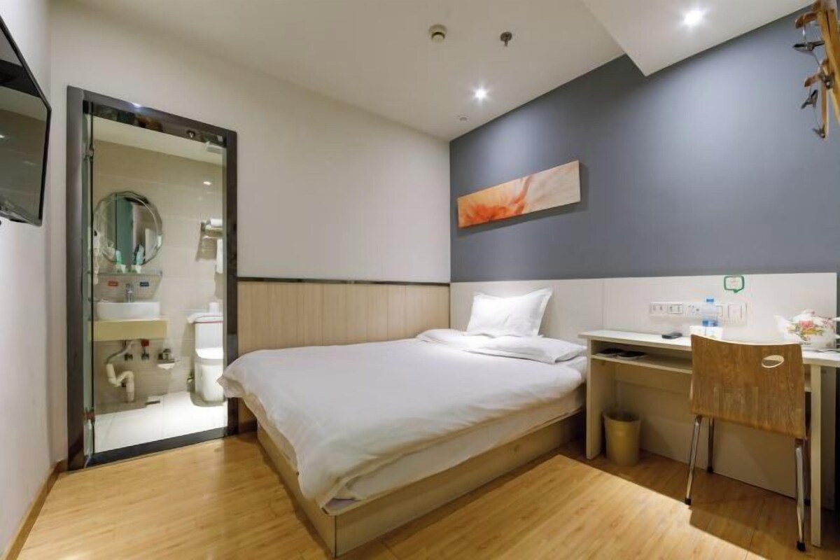 Habitación de hotel moderna con cama, escritorio, silla y baño visible a través de una puerta abierta.