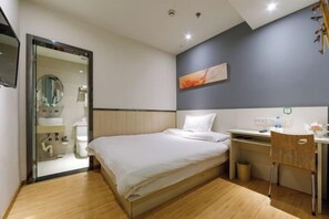 Habitación de hotel moderna con cama, escritorio, silla y baño visible a través de una puerta abierta.