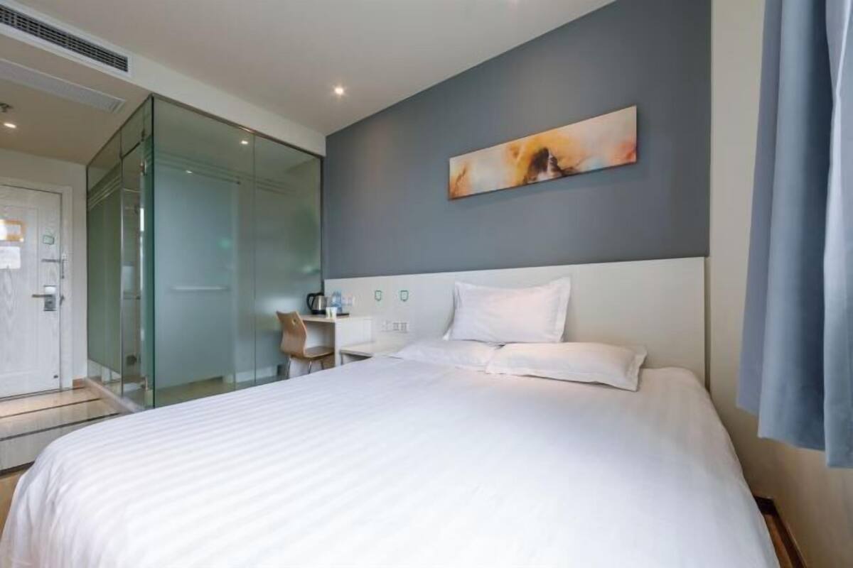 A hotel room with a bed, a desk, a chair, and a glass partition.