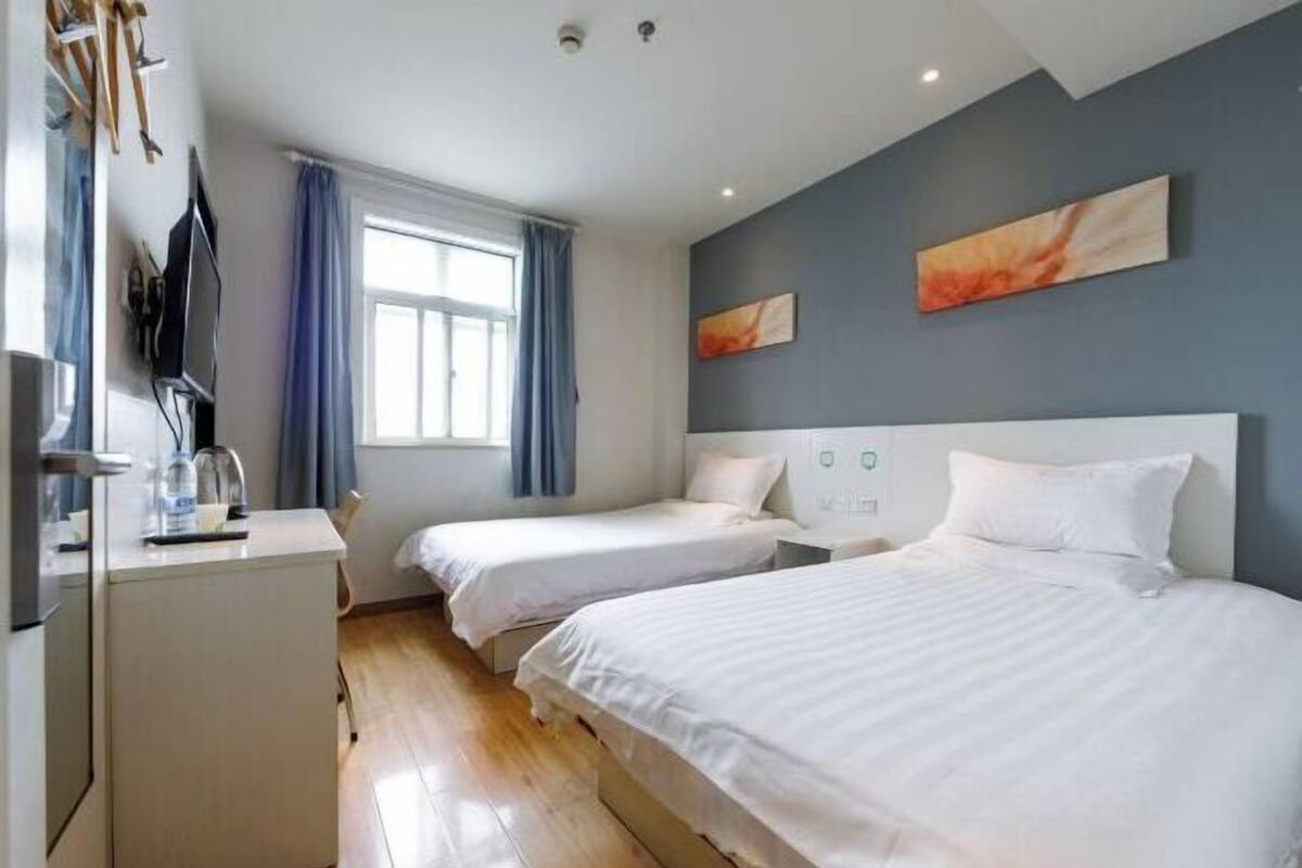 A hotel room with two beds, a desk, a TV, and a window with curtains.