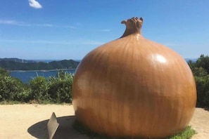 A large, spherical sculpture on a sandy surface with a clear sky and distant hills in the background. - Awaji Central Room NC03 (Awaji)