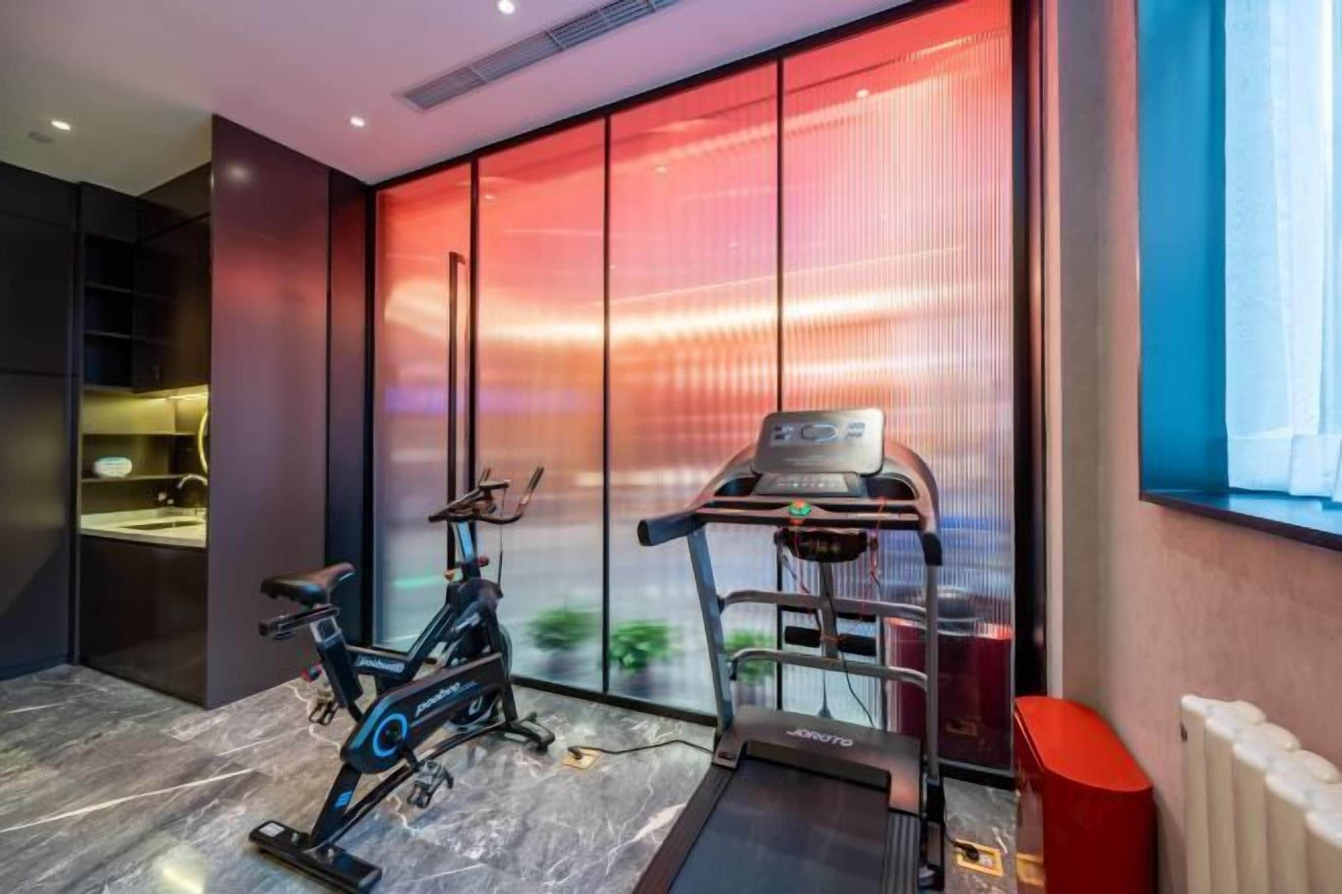 A modern gym with a stationary bike, treadmill, and a wall-mounted exercise machine.