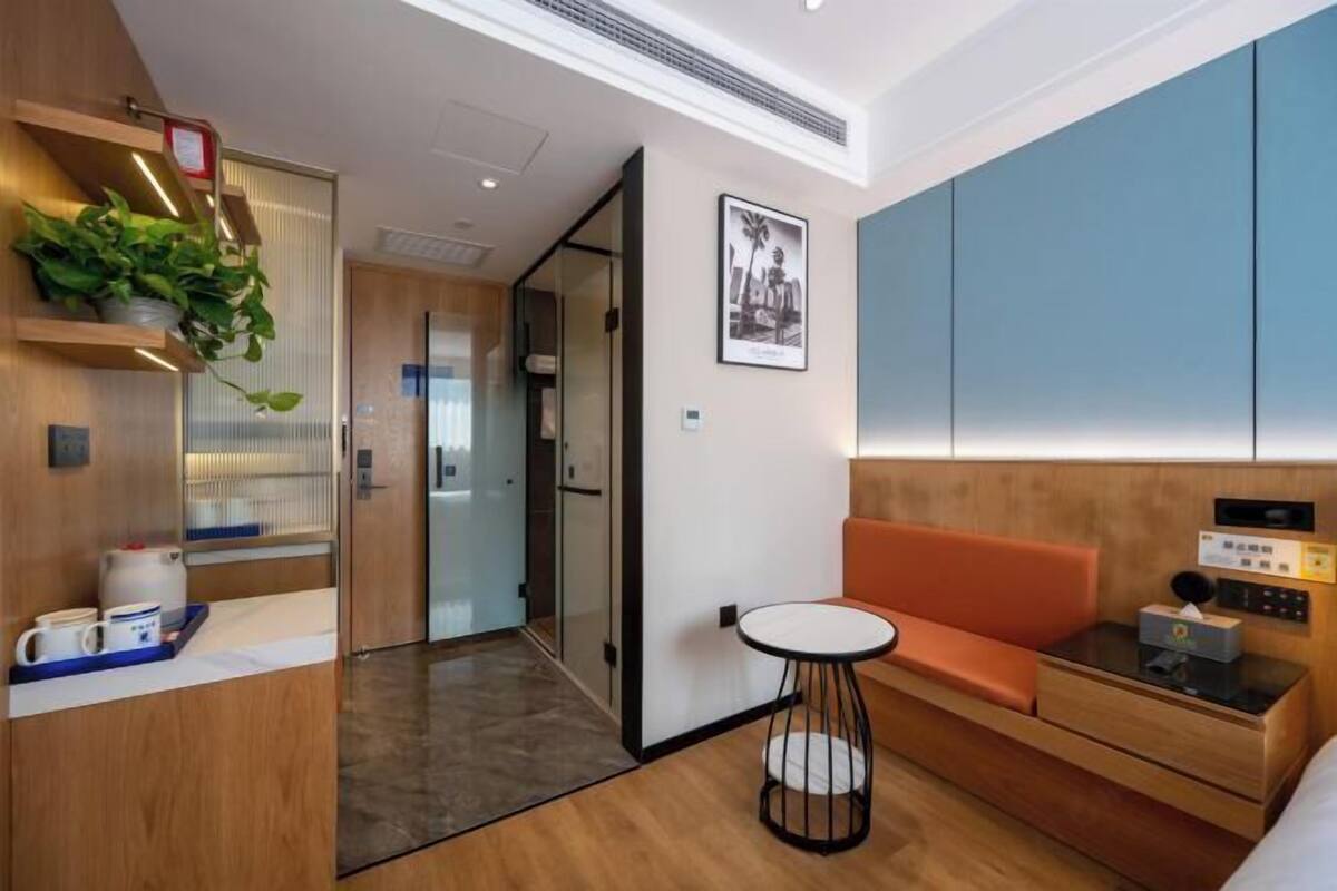 A modern hotel room with a wooden reception desk, a small round table, a sofa, and a bed.