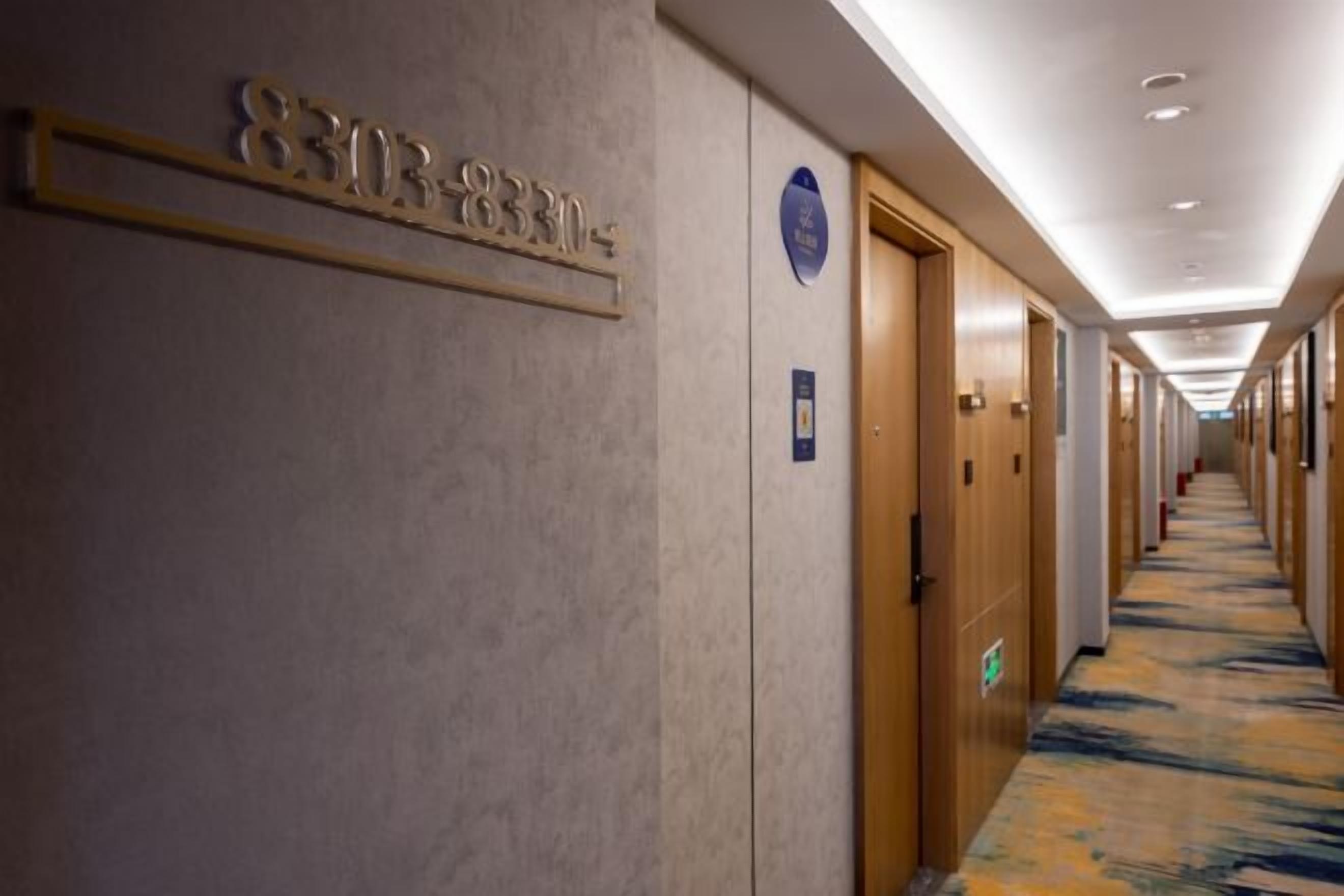 A hotel corridor with doors, a carpeted floor, and a sign with a phone number.
