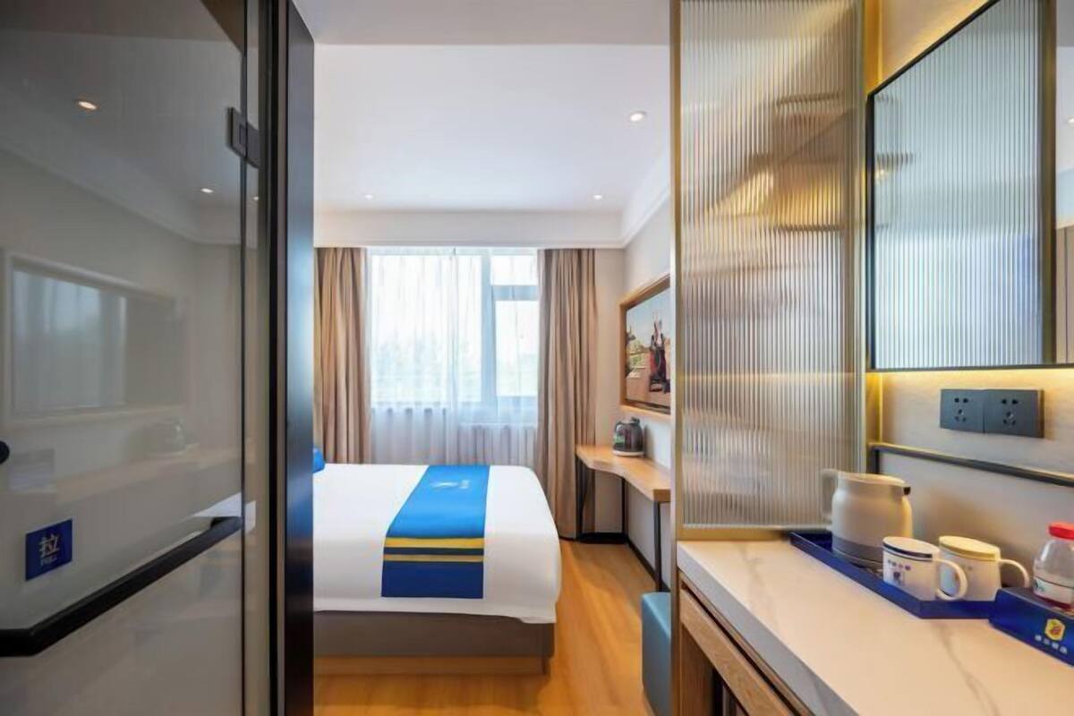 A hotel room with a bed, a desk, a coffee maker, and a tray with mugs.