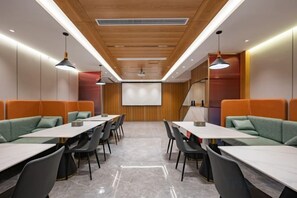Ein Konferenzraum mit einem langen Tisch, mehreren Stühlen und einer Leinwand im Vordergrund.