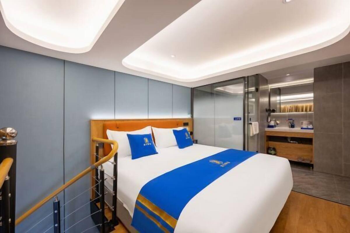 A modern hotel room with a large bed, a wooden headboard, and a blue accent wall.