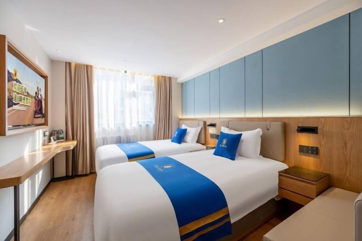 A hotel room with two beds, a desk, a nightstand, and a large window with curtains.