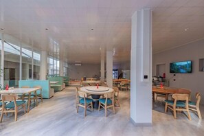 A spacious indoor area with multiple tables and chairs, a large pillar, and a television on the wall.