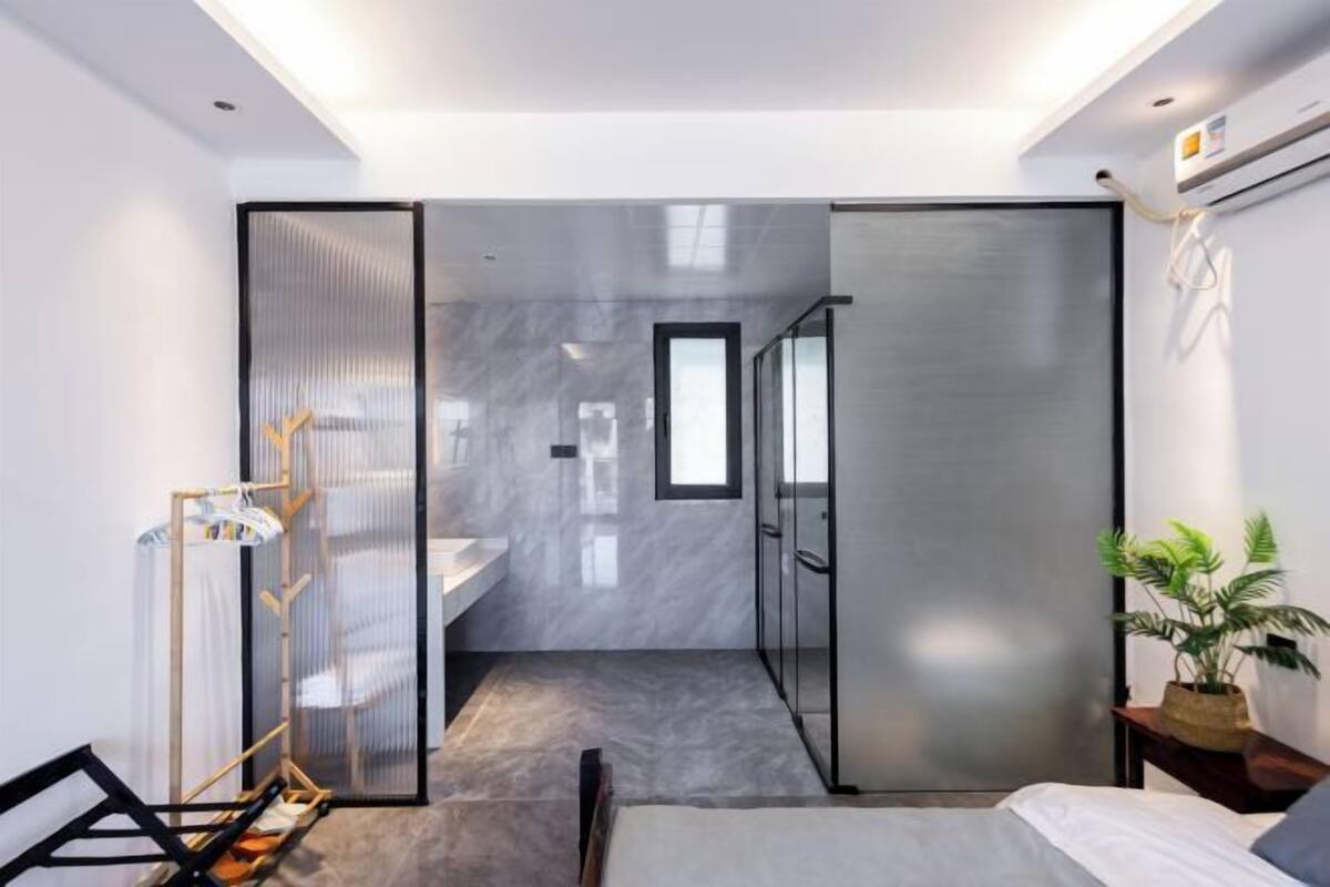 Habitación de hotel moderna con una cama, una mesita de noche, una planta y vistas al baño.