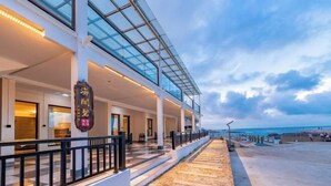 Un hotel con fachada de vidrio, zona de estar al aire libre y vistas al mar.