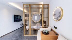 Una habitación moderna con cama, separador de madera, televisor y un cuadro colgado en la pared.