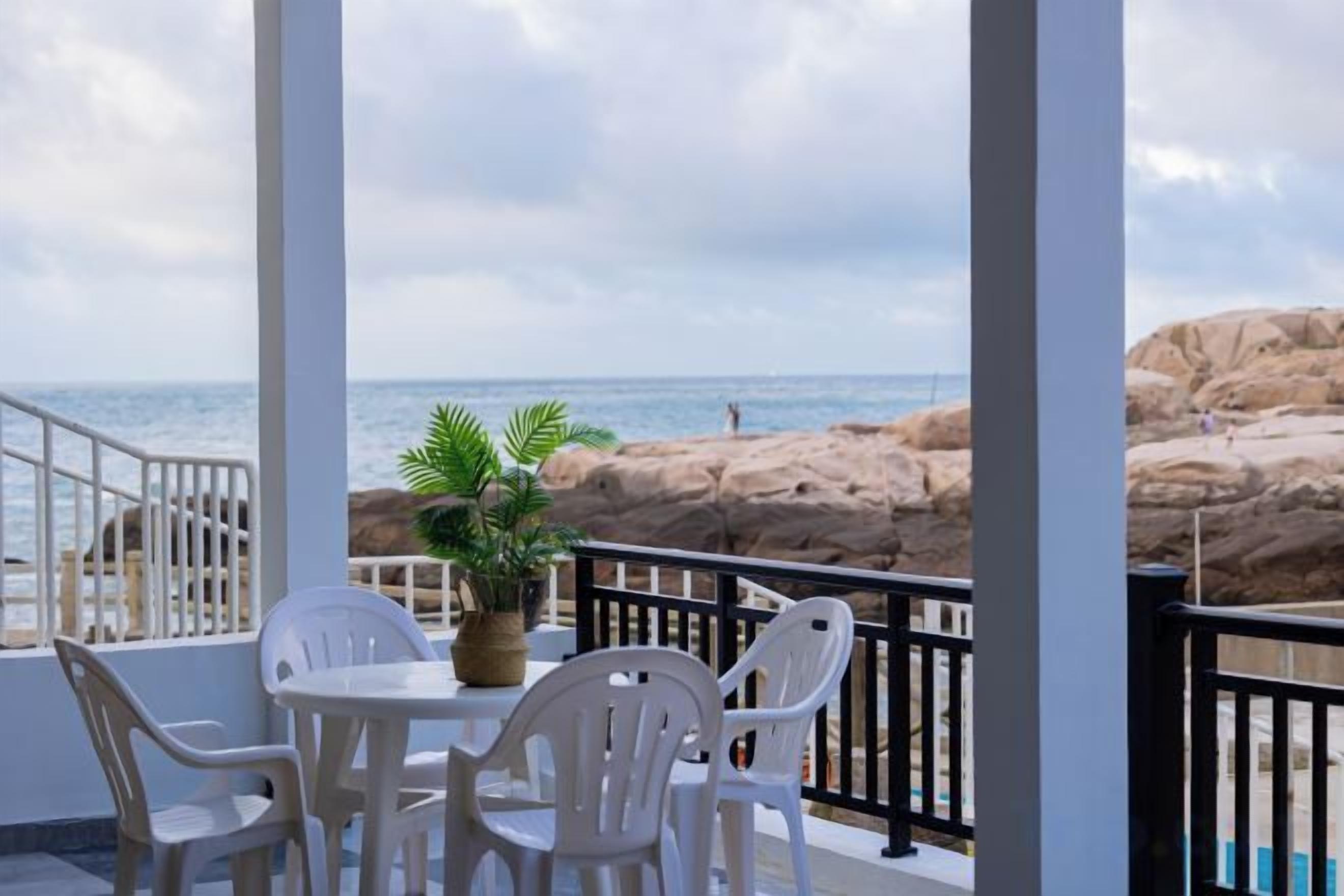 Un balcon avec des chaises blanches et un pot de fleurs, donnant sur une côte rocheuse et la mer.
