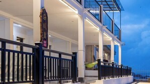 Fachada moderna de un hotel con estructura de vidrio, barandal de metal negro e izado con una bandera que tiene texto.