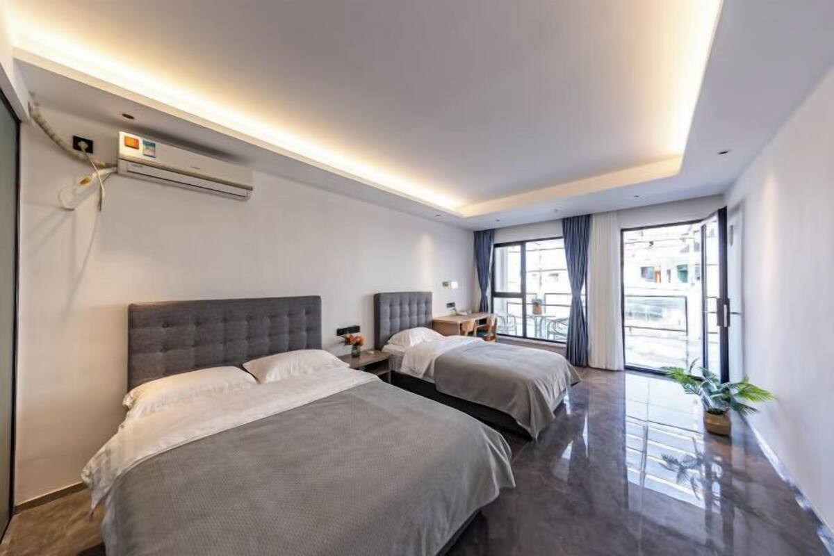 Una habitación de hotel moderna con dos camas, un ventanal grande y un equipo de aire acondicionado.