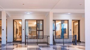 Un vestíbulo de hotel con piso de cuadros, puertas de vidrio que dan a las habitaciones y una barandilla central.