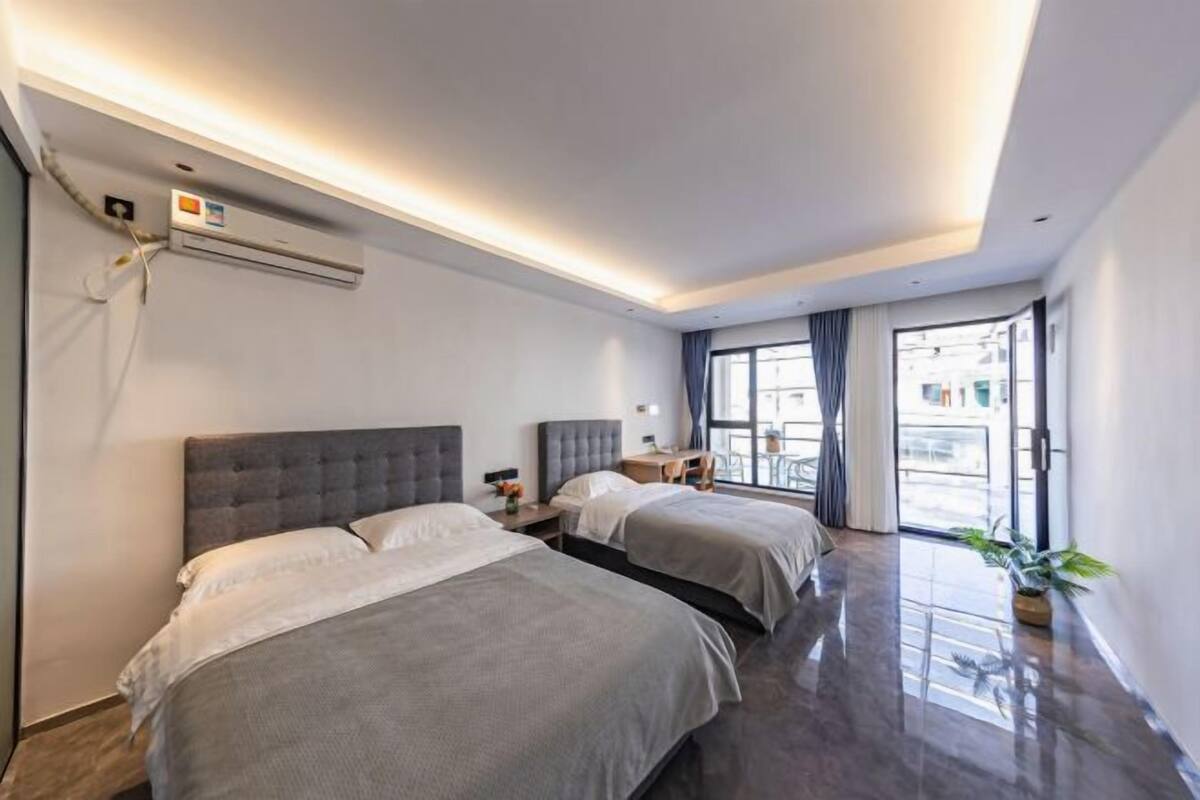 Habitación de hotel con dos camas, aire acondicionado instalado en el techo, una mesita con lámpara y vistas al exterior a través de amplias ventanas.